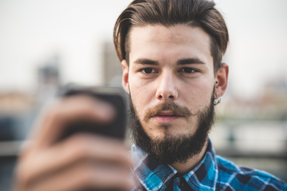 So gelingt dir das perfekte Bart-Selfie: Junger Mann macht ein Selbstportrait mit dem Handy